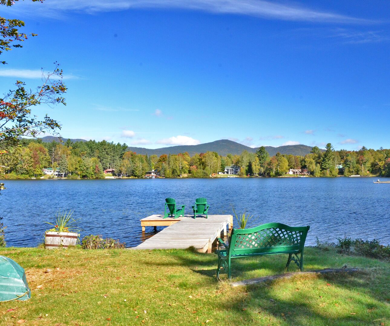 The wooden dock with green Adirondack chairs and bench overlooking Mirror Lake in Lake Placid, NY