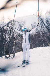 Female skier on the summit of Whiteface Mountain holding her poles up in the air